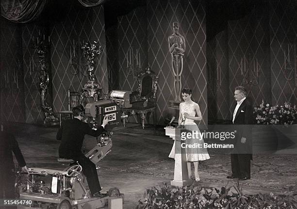 New York-: Audrey Hepburn smiles sweetly as she receives Hollywood's highest accolade--an Oscar for the best performance by an actress--from Jean...