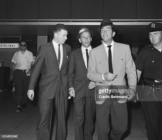 Photo shows Frank Sinatra and Dean Martin walking through lobby of airlines terminal upon their arrival from London. A reporter walks along on the...