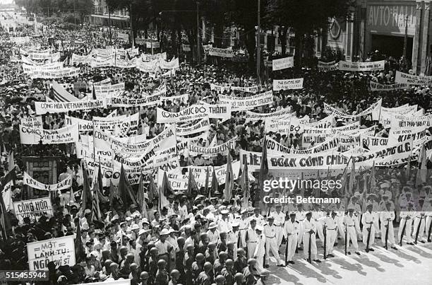 Banner and flag-carrying crowds march past the official residence of their new leader Ngo Dinh Diem to celebrate his overwhelming victory in the...