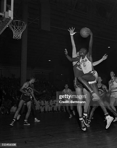 All American Bill Russell, , stretches his 6 ft. 10 in. Frame past guard of USC's Jim Sterkel for another two points for USF in 2nd period here....