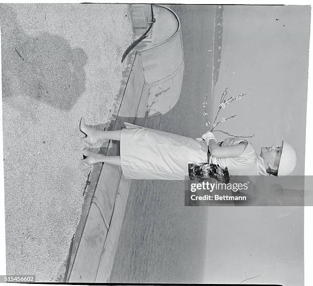 Actress-columnist-dress designer Gloria Swanson models her latest contribution to the fashion world, a pale beige shantung sheath with a side slit....