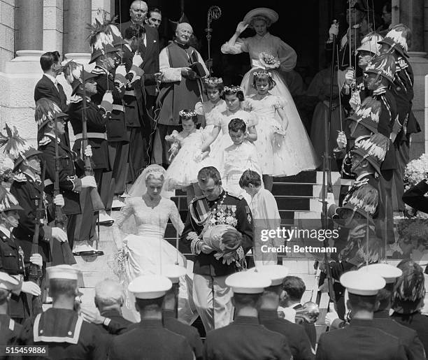 Surrounded by men in uniform Prince Rainier and Princess Grace leave the Cathedral of St. Nicholas, followed by the two page boys and four flower...