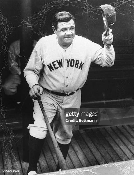 Babe Ruth is shown in this close-up, standing in the dugout holding his bat and waving his hat.