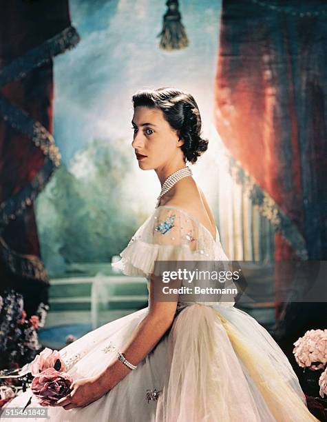 Princess Margaret Rose of England, is shown here seated and wearing a formal evening dress with sequence butterflies around the shoulder, and holding...