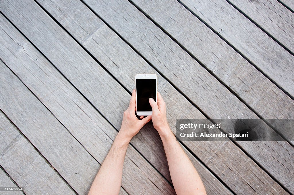 Hands holding mobile phone against wooden background