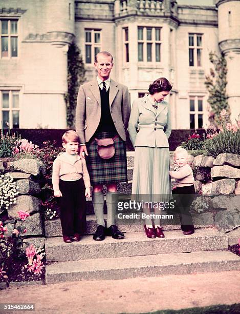 The Queen is seen in pleated skirt and close-fitting, three-button jacket. The Duke of Edinburgh is in kilts with Prince Charles and Princess Anne in...