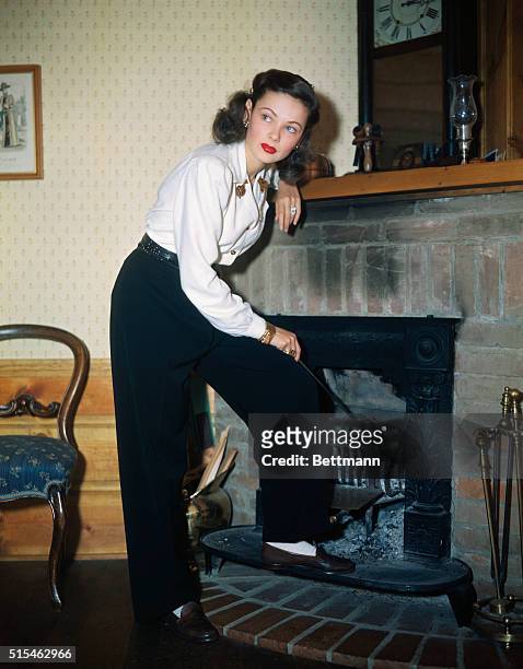Actress Gene Tierney is shown tending to the coals in a fireplace. Undated.