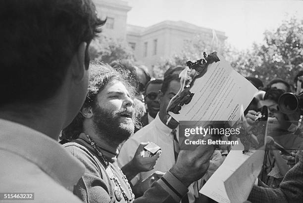 Yippie leader Jerry Rubin burns a newspaper copy of Mayor Richard Daley's report on the riots, 9/9, entitled "The Strategy of Confrontation." The...