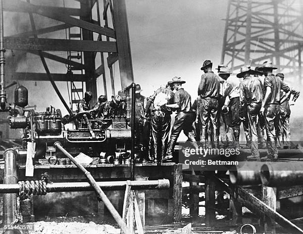 Oil well gushes 10,000 barrels daily; while crew trys to valve it. Beaumont? Texas: Photo show the oil-soaked crew desperately fighting to bring...