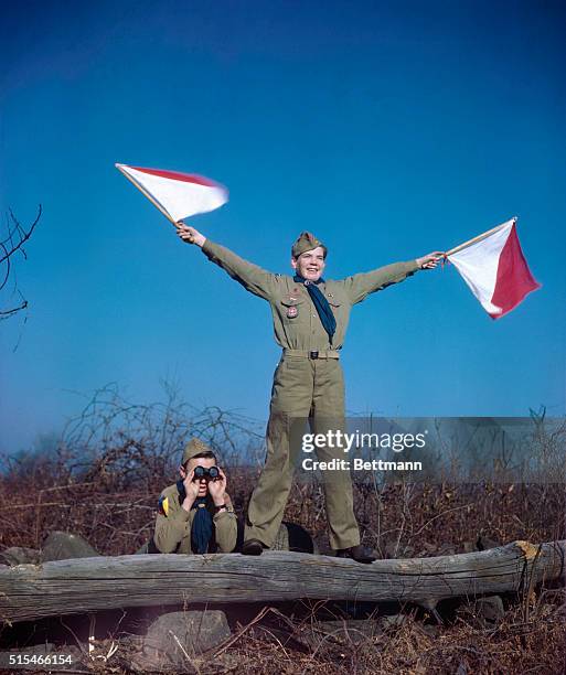 Boy Scouts on Camping Trip- Here, a scout is performing semaphore while another boy looks off to the distance with binoculars.