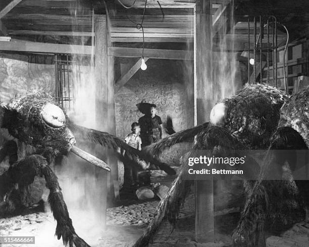 Dick Bellis and Scotty Correll cower behind two giant ants in a scene from the 1954 science fiction thriller, "Them]"