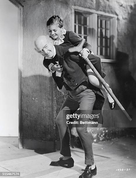 Movie still from the 1938 Metro-Goldwyn-Mayer production of A Christmas Carol where Scrooge is carrying Tiny Tim on his back.
