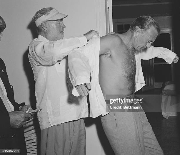 Writer Ernest Hemingway helps his friend, actor Gary Cooper, into something more comfortable and appropriate, after his arrival in Cuba as the...