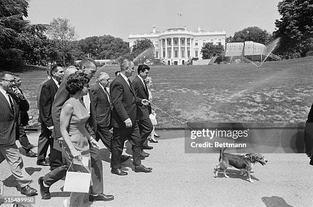 President Johnson and his pet Beagles, Him and Her, lead members of the White House Press Corps during an afternoon stroll today. In background is...