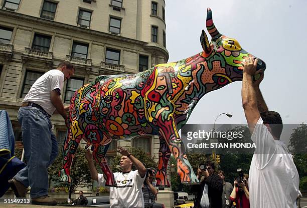 Life-sized fiberglass cow painted by an artist named "Billy" is lifted by workmen off a truck in front of the Plaza Hotel in New York 15 June 2000 as...