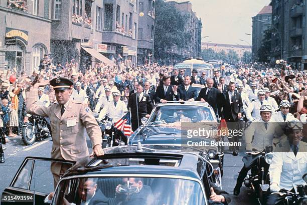 The motorcade of President Kennedy, Chancellor Konrad Adenauer, and West Berlin Mayor Willy Brandt makes its way through cheering crowds after the...
