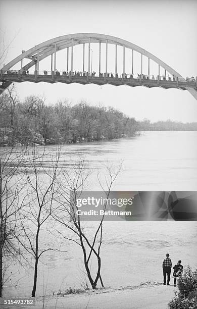 March 21, 1965 - Selma, Alabama: Lone Selma resident stands on bank of Alabama river and watches long line of racial demonstrators silhouetted...