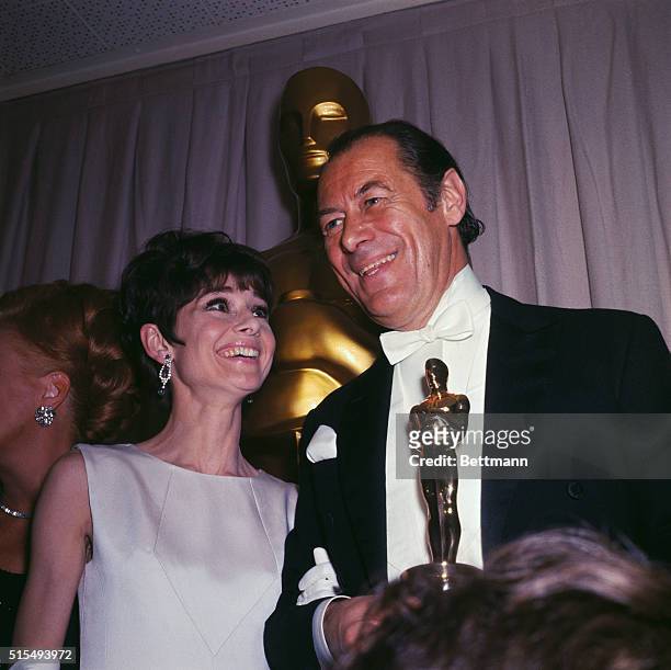 Oscar winner Rex Harrison poses with Audrey Hepburn during the 37th annual academy Award presentations..