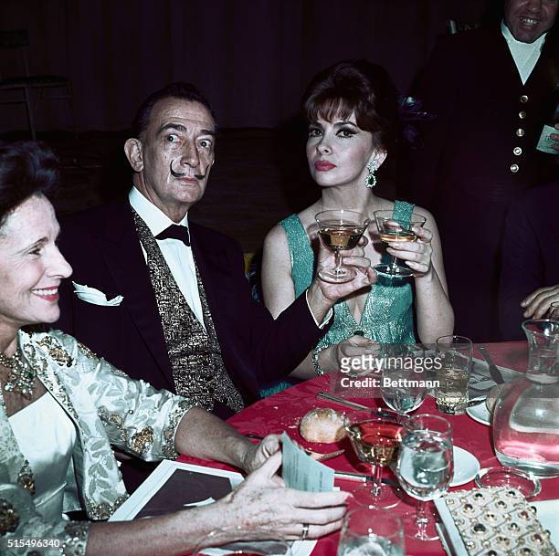 Moustached artist Salvador Dali and lovely Gina Lollobrigida raise glasses together here at a party following the premier of The Sound of Music held...