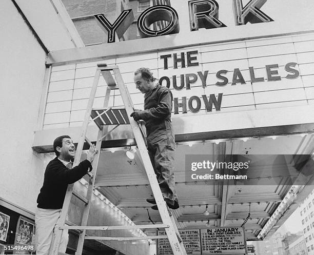 Comedian Soupy Sales standing on a ladder talking to man working on the marquee at the York Theater, where the Soupy Sales show is featured.