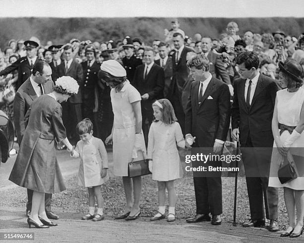 The Queen of England shakes the hand of four-year-old John F. Kennedy Jr. As she and Lord Harlech, former ambassador to the US, greet members of the...