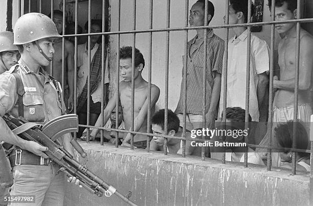 Soldier watches suspected Communists held at Tangerang, a suburb of Jakarta. Many suspected Communists have been taken into custody since the recent...