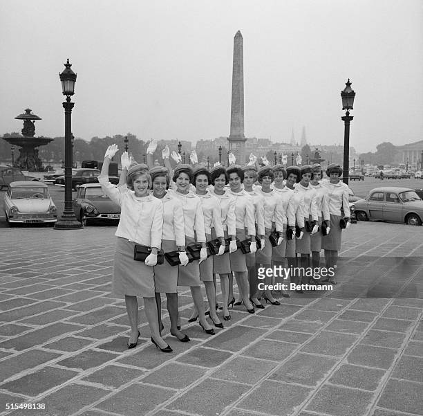 Donned in their new uniforms, designed by couturier Pierre Balmain, a group of new Trans World Airlines hostesses wave in unison on the Place de la...