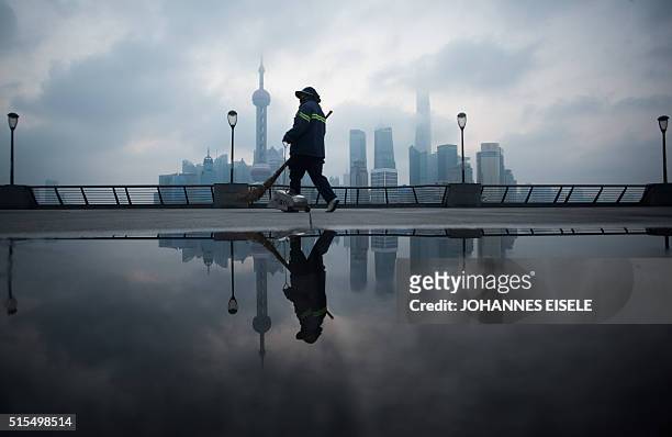 Street cleaner walks by the bund near the Huangpu river across the Pudong New Financial district, in Shanghai on March 14, 2016. China's leaders are...