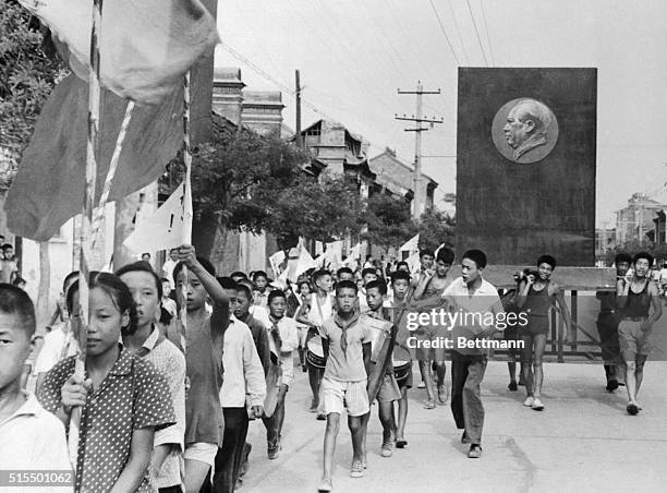 Carrying flags and beating drums, Communist China's Red Guards march through a street in Peking. The youths also display a huge portrait of their...