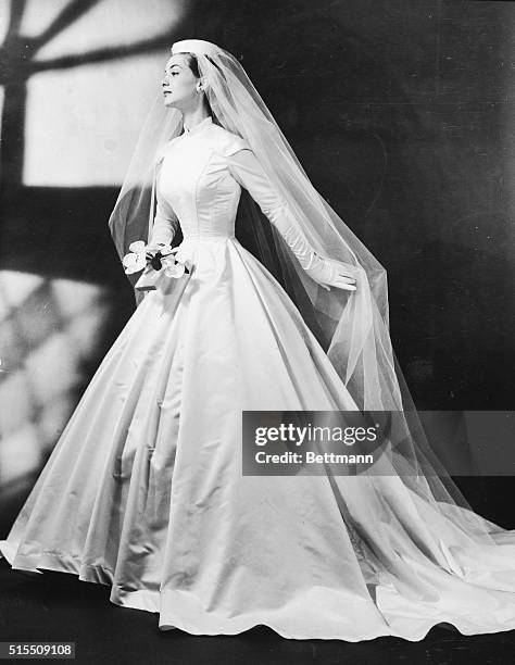 Wedding gown: Demure and dignified, smooth-fitted plastron bodice with tiny standing collar, epaulettes at shoulders, Cathedral train, in Celanese...