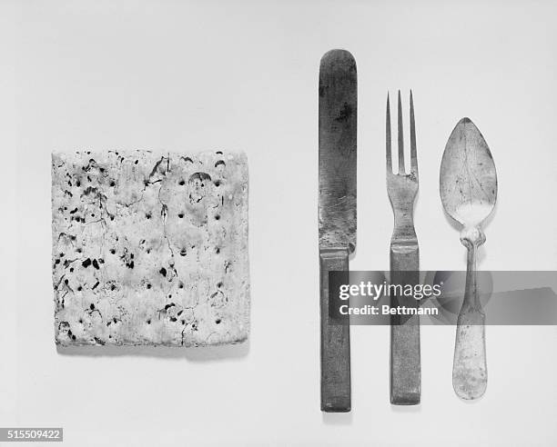 Butter knife, fork, and spoon from the mess kit of a Union soldier alongside a hardtack, bread made from only flour and water.