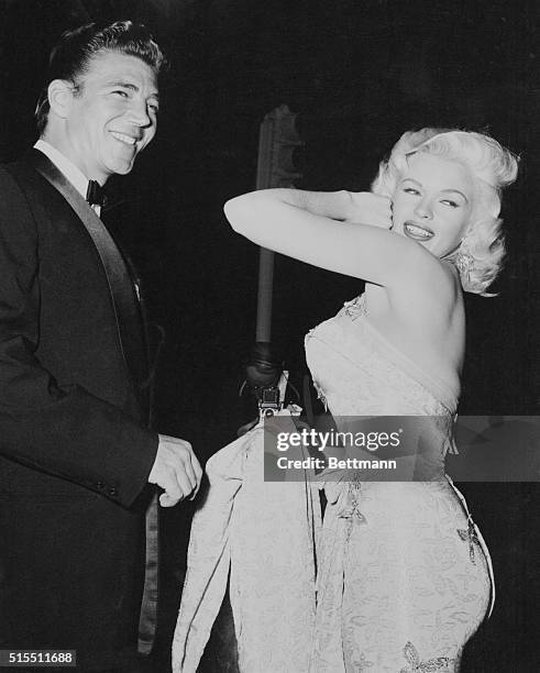 American actress Jayne Mansfield escorted by Mickey Hargitay in a specially designed gold gown which she is showing off to the photographers and...