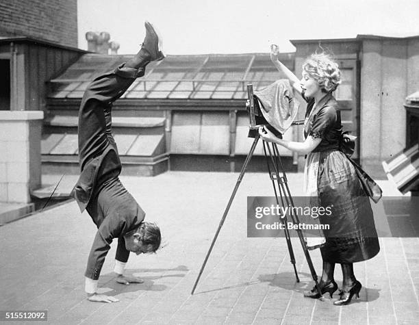 Mary Pickford takes a picture of husband Douglas Fairbanks, Sr., who is executing a handstand on the roof of a building, .