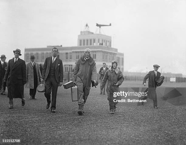 Colonel Lindbergh carries the baggage as he and Mrs. Lindbergh walk to their plane at the East Boston, Massachusetts, Airport to take off for their...