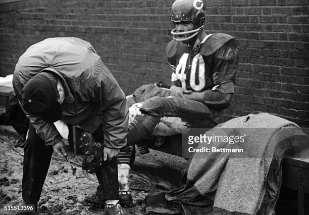 Trainer cleans muddy spikes of fleet Chicago Bears HB Gale Sayers during 4th quarter of the game with San Francisco 49ers here 12/12. Rookie Gale...