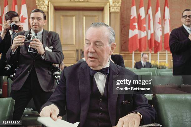 The Prime Minister of Canada, Lester Pearson is shown closeup as he is seated at a desk going through papers.
