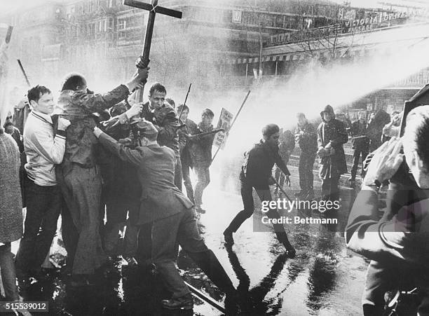 Policemen try to hold back a mob of cross carrying students as a powerful jet from a water cannon is applied to the demonstrators from the right....
