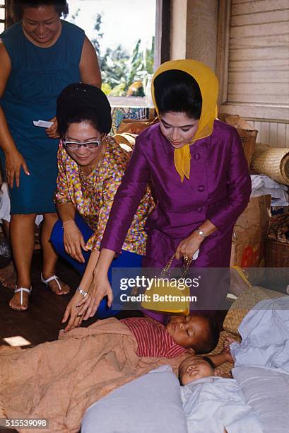 Mrs. Imelda Marcos, wife of President Ferdinand Marcos of the Philippines, gets acquainted with a tiny tot during visit to evacuation center in...