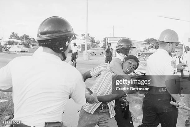 August 8, 1968 - Miami: Miami policemen, one holding the man's arm and the other with an arm lock on his neck, drag away a Negro youth during a clash...