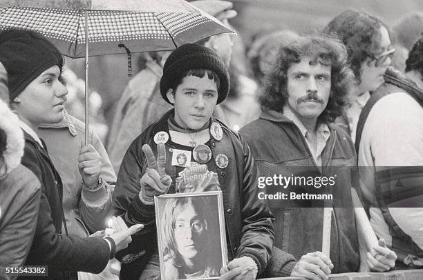 Keeping vigil 12/8 outside the Dakota apartment where former Beatle John Lennon was shot to death a year ago, a youngster holds a photo of Lennon...