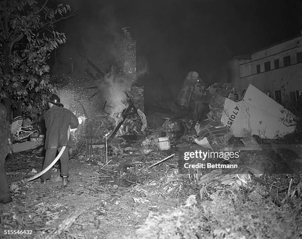 Fireman attempts to extinguish flames from the wreckage of Howard Hughes' XF-11 plane which struck and set afire three houses and a garage before it...