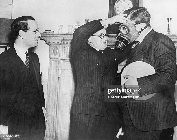 Wendell L. Willkie is fitted with a gas mask in the home office by Herbert Morrison, the Home Secretary, while Malcolm MacDonald looks on. Under...