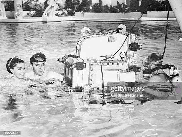 Mermaid movie star Esther Williams listens to explanations from director George Sidney about the underwater camera that will photograph the actress...