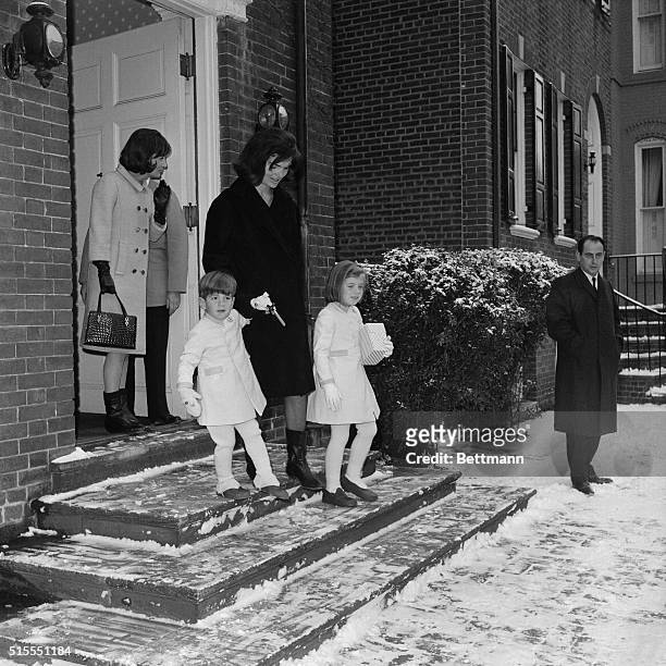 Mrs. Jacqueline Kennedy, accompanied by her children, John Jr., and Caroline, emerge from their home, en route to Andrews Air Force Base. From there...