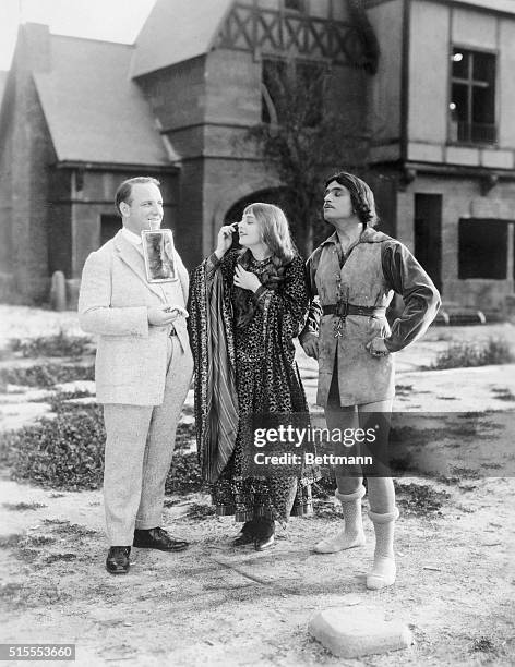 Preparing For New Picture. Allan Dwan poses as the pedestal for Miss Enid Bennett's mirror. And Douglas Fairbanks, featured in a pair of tights,...