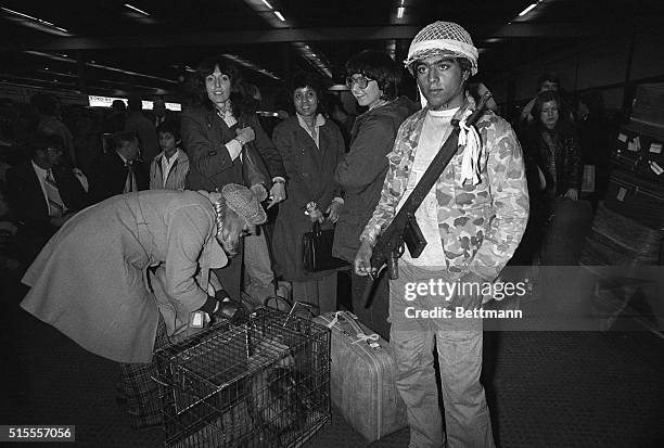 Guerrilla loyal to the Ayatollah Khomeini stands guard 2/17 as American evacuees get their luggage ready to board flights taking them to Rome and...