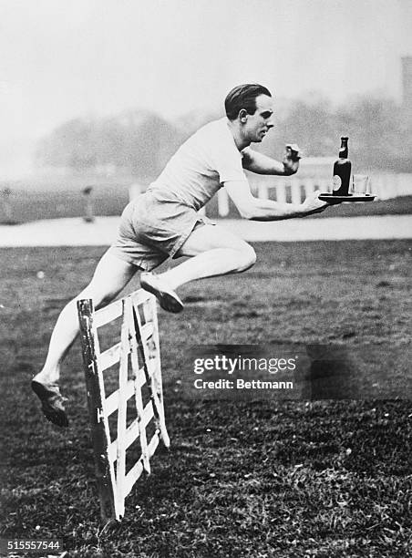 Hodge, the crack British hurdler and cross country runner, is shown above making a perfect leap over the hurdles while carrying a tray and bottle....