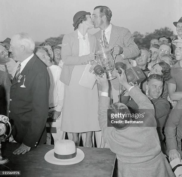 Tony Manero, Greenboro, N.C., pro, holds the championship cup as Mrs. Manero plants a resounding kiss after the little known Italian had won the U.S....