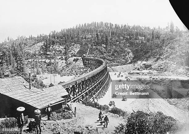 Chinese laborers at work with pick and shovel wheelbarrows and one horse dump carts filling in under the long secret town trestle which was...