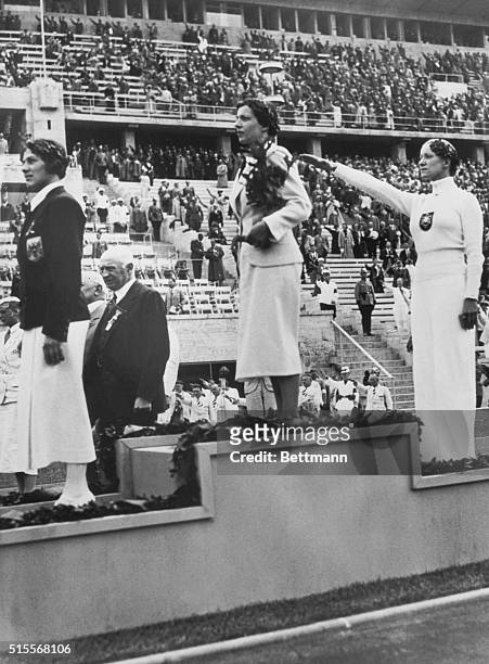 The three winners of the Women's Individual Foil competition in the 1936 Olympic Games stand on the podium in Berlin as spectators applause. : Bronze...